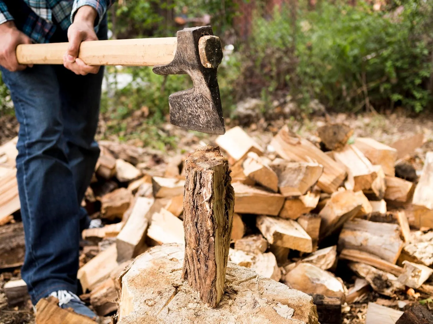 How to Remove a Tree shown with a man using an axe to split a tree stump into firewood, demonstrating safe and practical tree removal methods.